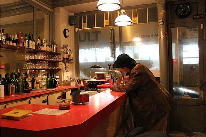 photo de spectacle une jeune femme costumée en homme écrit assise au comptoir d'un bar