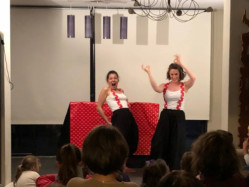 deux comédiennes en tee shirt blancs pantalons noirs et bretelles rouges à pois blancs jouent un spectacle devant un public elles se font piquer par des abeilles