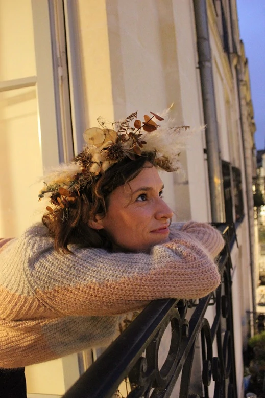 jeune femme avec une couronne de fleurs sur la tête accoudée à un balcon qui regarde rêveusement le ciel
