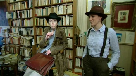 photo de spectacle deux comédiennes costumées en hommes des années 50 pantalon chemise bretelles et chapeaux discutent dans une bibliothèque
