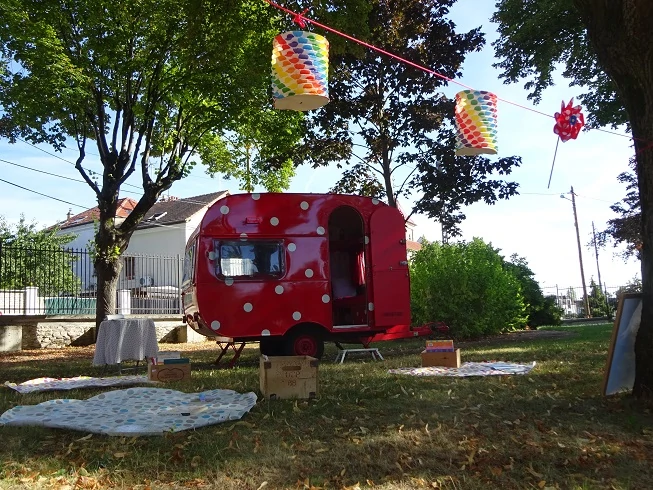 photo d'une caravane rouge à pois blancs au milieu d'un parc avec des lampions