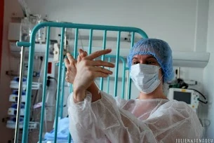 une jeune femme à l'hôpital avec une blouse une charlotte etun masque raconte une histoire à doigts avec ses mains elle sourit